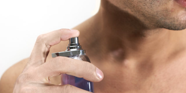 Barechested man with cologne bottle, close-up, mid section