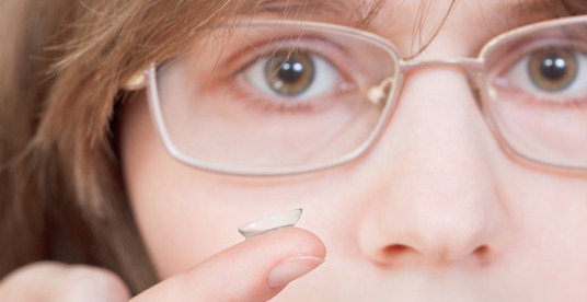 girl with glasses holds contact lens on your finger near the eyes